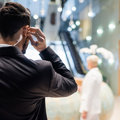 back view of bi-racial security man adjusting earpiece near blurred businesswoman and african american bodyguard.